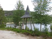 Klokkestøpulen på Lønnegrav gravplass. Bedehuset på andre sida av vatnet. (Foto: Olav Momrak-Haugan, 2010.)