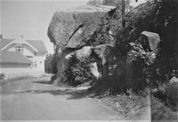 Lundesteinen på Nærsnes 1932. På dette tidspunktet er spissen (ned til venstre) på steinen fjernet for at busser skulle kunne passere ned til Isachsenbrygga. Lundes butikk i bakgrunnen med lagerbygget nærmest. (Foto fra Knut Erik Wennerslund)