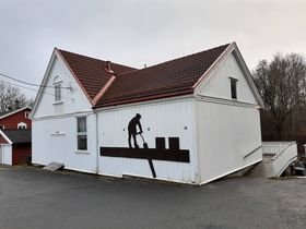 Nærsnes Grendehus, den gamle skolen fra 1922, har isskjæreren på veggen. Isskjæreren er laget etter et bilde av Oscar Ellefsen som skar is på Schwartzedammen. (foto: Ragnar Vadseth)