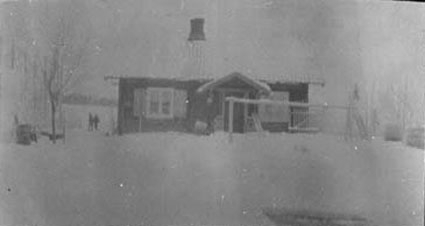 Uskarpt bilde av husmannsplass der vi ser et enkelt hus med to vindu, inngangsparti og pipe.