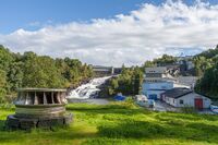 Øvre Leirfoss kraftverk med en horisontal francisturbin utstilt i forkant. Kraftverket åpnet i 1901, ombygget til et småkraftverk i 2014. Foto: Dag Endre Opedal/Norsk Vasskraft- og Industristadmuseum (2012).