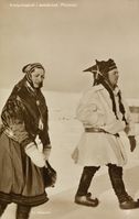 Bildet er tatt under kronprinsparets reise til Finnmark våren 1934. Kronprinsesse Märtha (til venstre) og kronprins Olav går i et snødekka viddelandskap. Begge er kledd i Kautokeino-drakt(?), han er iført pesk av reinskinn. Foto: Nasjonalbiblioteket