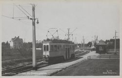 Holtet med billettboden i bakgrunnen. Fotografen står med ryggen til verkstedhallen og ser mot byen. Sporsløyfen kommer tilbake inn fra høyre og går bak billettboden. Foto: Nasjonalbiblioteket (1920-1925).