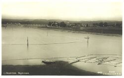 Utsikt fra Rælingen mot Nitelva med Nybrua i bakgrunnen. Lillestrøm ligger til høyre. Bildet er hentet fra Nasjonalbibliotekets bildesamling.