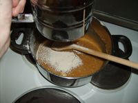 Tørrvarene blir sikta i gjennom mjølsikt. Kasserollen er teken av den varme kokeplata til han kolnar noko — hjortesaltet skal ikkje utsettast for sterk varme føre peparkakene blir steikt.