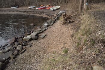 I vannkanten innerst kan du se gule ballastsein, en type stein som ikke naturlig hører hjemme her. Hele vegen som går langs vannet, er bygd opp av ballastsein som er sikret med en mur av større steiner mot vannet. (foto Victor Iversen 2021)