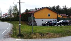 Bilde ved kryss Branderudveien/Asak kirkevei. Sverdkopi plassert høyt i stolpen for å unngå hærverk, pekende mot gravfeltet.