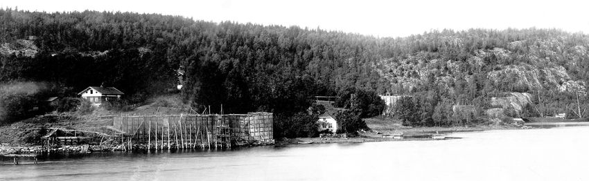 LASTEBRYGGE OG ISSTABLER PÅ BRYGGEBAKKEN OG GRAFFODDEN 1890-ÅRA. Lengst til venstre ligger det som senere ble kalt "den lille isbrygga. Eiendommen bak brygga er Bryggebakken. Isstabelen på Bryggebakken er midt på bildet. Dette var den eneste isstabelen der skutene kunne legge helt inntil for å laste is. Delvis skjult av trærne er Syverstadgården. Eiendommen midt på bildet er Odden, der Røyken Seilforening holder til i dag. I bakgrunnen ser vi den store og den lille isstabelen på Graffodden. På stranda foran stablene ser vi tre landfester for skip, laget av tømmer og fylt med stein. Til høyre, i Grundvik, ligger lastebåten Mimi. (Foto fra AS Søndre Nærsnes, fotograf ukjent)