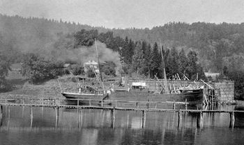 DAMPSKIPET A DEKKE LASTER IS 1894-1902 liggende ved Bryggebakken. Skuta ligger høyt i vannet og venter sannsynligvis på islast. Bak og til høyre for skipet sees isstabelen på Bryggebakken. Bak denne isstabelen sees toppen av isstabelen på Graffodden. De nærmeste bryggene (isrennene) kommer fra isstablene på Mellomstranda og Flatstranden. Bildet er et utsnitt av et større bilde. (Foto AS Søndre Nærsnes)