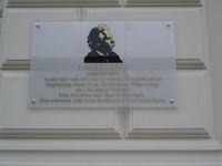 Plakett med Edvard Griegs portrett på forleggernes hus i Leipzig.