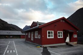 Ei skule. Husa er malt raude. Utafor er det ein asfaltert leikeplass.