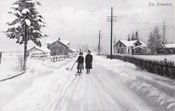 Skitur på Gamle Strømsvei rundt 1920. I bakgrunnen går Korsveien forbi Stalsberghagen gravlund inn i Rælingen kommune. I huset til høyre hadde Alf H. Fossum kolonialbutikk. Dette huset ligger i Rælingen, husene på venstre side ligger i Strømmen.