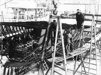 M/F Haalogaland under bygging.Erik Eriksen står øverst og er «mannevekt» sammen med ukjent for å styre hudplata inn til spant. Foto ukjent, utlånt av Anny Sørensen.