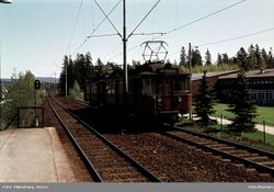 Østgående tog har forlatt stasjon, sett fra vestgående perrong. Deler av daværende bygnineger til Persbråten videregående skole til høyre. Foto: Sverre Okkenhaug/Oslo Museum (1978).