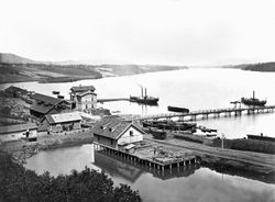 Oversiktsbilde med Eidsvoll stasjon, to dampbåter, beddingen med to klinkbygde lektere og brua over Vorma. Kilde: Jernbanemuseet