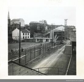 Byggingen i juli 1951: Sett mot nord, med Jordal idrettsplass i høyre bildekant med en trapp inn til tribunen, grusbanen fra 1937/1938 («Bingen») til venstre. Det hvite murhuset ved «Bingen» er Hølandsgata 31 og Hølandsgata 40 til høyre bak, begge revet i 1956-1958. Foto: Arbeiderbevegelsens arkiv og bibliotek (1951).