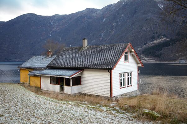 Jordal skulehus. Ei kvitmalt stove på grunnmur av stein. Gult hus i bakgrunnen. Bilde tatt med utsikt mot fjorden.
