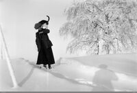 Kvinne med katt på skulderen. Skygge av fotografen i snøen.