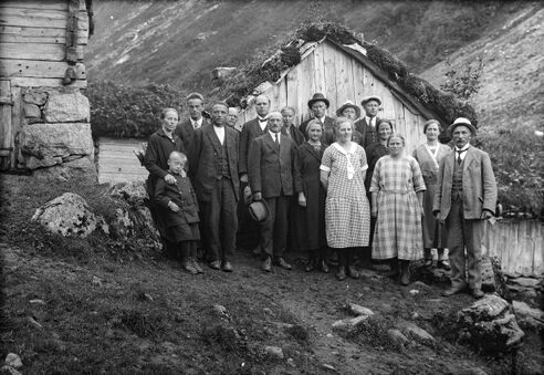 Ei gruppe lærarar og ein liten gut ståande forran eit lite støylhus med torvtak.