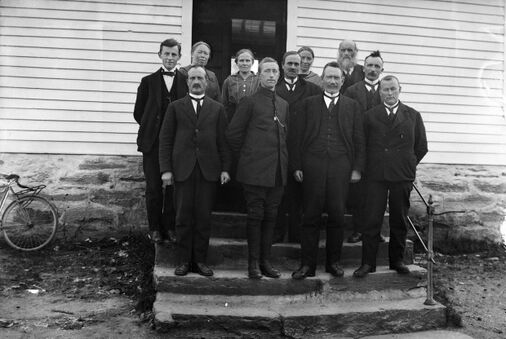 Svart-kvitt foto av 11 lærarar som står på ei trapp.