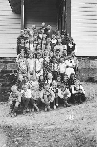 Gruppe born og nokre vaksne forran eit skulehus.