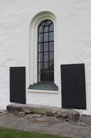 To gravplater i metall fra 1769 er innfelt i kirkens østvegg. De lå opprinnelig på kirkegården rett bak koret sammen med to andre plater, ifølge Schønning. Foto: Chris Nyborg (2014).