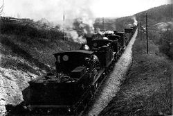 Brynsbakken har stigning på 26,6 ‰. Dette er Hovedbanens bratteste. Her sliter et tungt godstog seg oppover med lokomotiver i hver ende. Foto: Jernbanemuseet (1890).