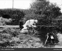 Klesvask i Losbyelva i Lørenskog kommune. I bakgrunnen Hammer bru. Mellom ca. 1910 og 1915.