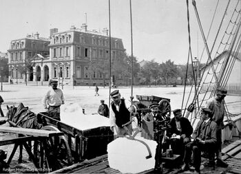 LOSSING OG VEIING AV IS I MARSELLES ca 1900 .Is losses fra en seilskute over til en hestekjerre i Saint-Nazaire i Frankrike. Mannskapet fra skipet står for lossingen. Isblokken i is-saksa veies på vekta på dekket før den laste om bord i hestekjerra. Ved siden av vekta sitter representanter for selger og kjøper og noterer vekten på lasta. I bakkant en tom hestekjerre som venter på tur for islast. (Foto Røyken Historielag, fotograf ukjent)