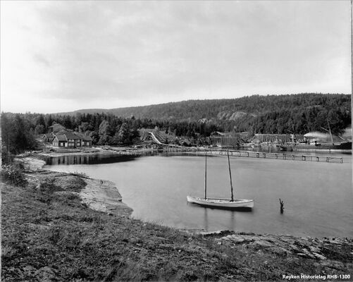 Nærsnesbukta 1893-1898. Isstabel ovenfor Mellomstranda med den lange isrenna ut i bukta. Det er isstabler og et permanent ishus (med saltak) på Flatstranda inn mot Bryggebakken. Dampbåt laster is ved den lille isbrygga ved Bryggebakken. Eiendommen Nærsnesstranden innerst i bukta. Gården ble revet rett for å gi plass til Teglverket i 1900. (Foto fra AS Søndre Nærsnes, fotograf ukjent)