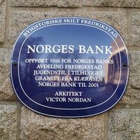 Blå oval byhistorisk plakett på steinvegg i Fredrikstad. Skiltet forteller om Norges Bank-bygningen, oppført i 1916 i jugendstil av hugget granitt, brukt som Norges Banks avdeling i Fredrikstad fram til 2001, tegnet av arkitekt Victor Nordan