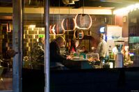 Interiøret sett gjennom vinduet, 2012. Bjørn Elvebredd jr. bak baren i samtale med gjester. Foto: Roy Olsen.