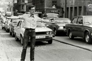 Pål Jensen står med armene utstrakt foran en lang kø av biler i en bygate