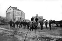 Personalet på Hamar stasjon oppstilt foran en vogn på bryggesporet med stasjonsbygningen i bakgrunnen 1862. Kilde Jernbanemuseet.