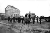 Personalet på Hamar stasjon oppstilt foran en vogn på bryggesporet med stasjonsbygningen i bakgrunnen 1862. Kilde Jernbanemuseet.