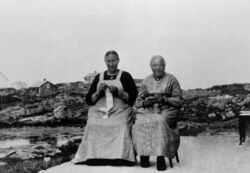 Ragnhild Rasmusd Husa (til venstre) og Agate Jamne, flittige med handarbeid. Bakom er Kopper med bedehuset i venstre biletkant, så bnr 2, bnr 37 og bnr 1 (dels bakom). Koppersevja ligg framme til venstre.