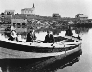 Omkring 1917. Frå venstre: Agnes (22b), Oluf (23), Elias (22) og Ola (21c) Ophaug. Oppe til venstre er løa til Stuberg. Ned til venstre er Gullak Grenden (15) sitt naust, der som ferjekaien er no. Elles ser me frå venstre kyrkja, løa til Muren, huset til Muren (bak), huset til Stuberg husmenn 3 og 4, torvhuset til Stuberg (framme).