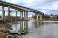 Under Sandesundbrua, midt i Glomma, går kommunegrensen mellom Sarpsborg og Fredrikstad. Den røde murbygningen i bakgrunnen er den gamle tollboden på Sandesund i Sarpsborg kommune. Foto: Leif-Harald Ruud (2020).