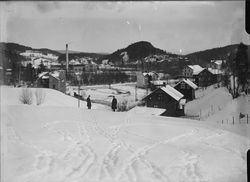 Hamang-området sett fra Bjørnegård-området, med Fabriken Tomten fra 1912 til venstre for mennene i bildet, og med Hamang Papirfabrikk fra 1907 bak denne. Sandvikselva bak trærne som går gjennom bildet. Bebyggelsen på denne siden av elva ligger til veien som i 1955 fikk navnet Industriveien. Foto: Narve Skarpmoen/Nasjonalbiblioteket (1912–1930).