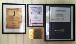 Diplomer for Strømlingenstatuetten, kommunens Byggeskikkpris og Rotarys æresbevisning henger i glass org ramme innenfor dørene. Foto Steinar Bunæs.