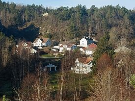 Bebyggelsen til tre av Vestre Våg-gårdene, de hvite bygningene til høyre i bildet, bnr 1 nærmest, deretter bak og litt til venstre bnr. 2 og bnr. 5 bakerst. Foto: Pål Giørtz (2025).